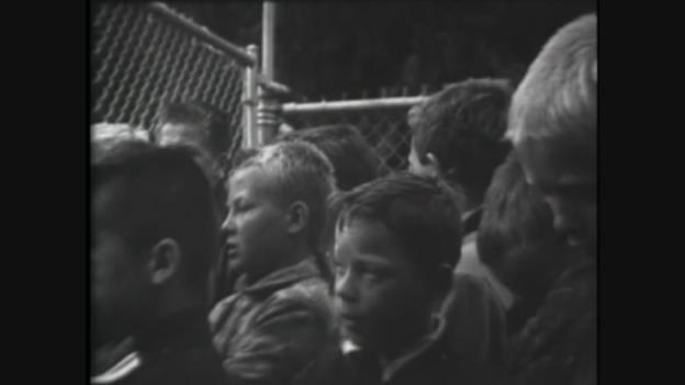 A black-and-white photo of boys behind a fence.