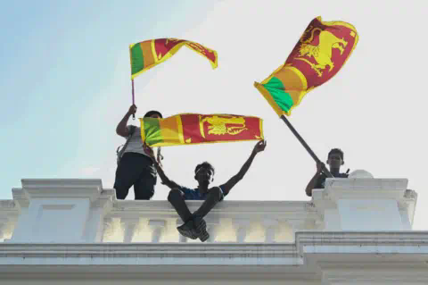 Getty Images Three young men wave Sri Lankan fans from atop a white co<em></em>ncrete balustrade
